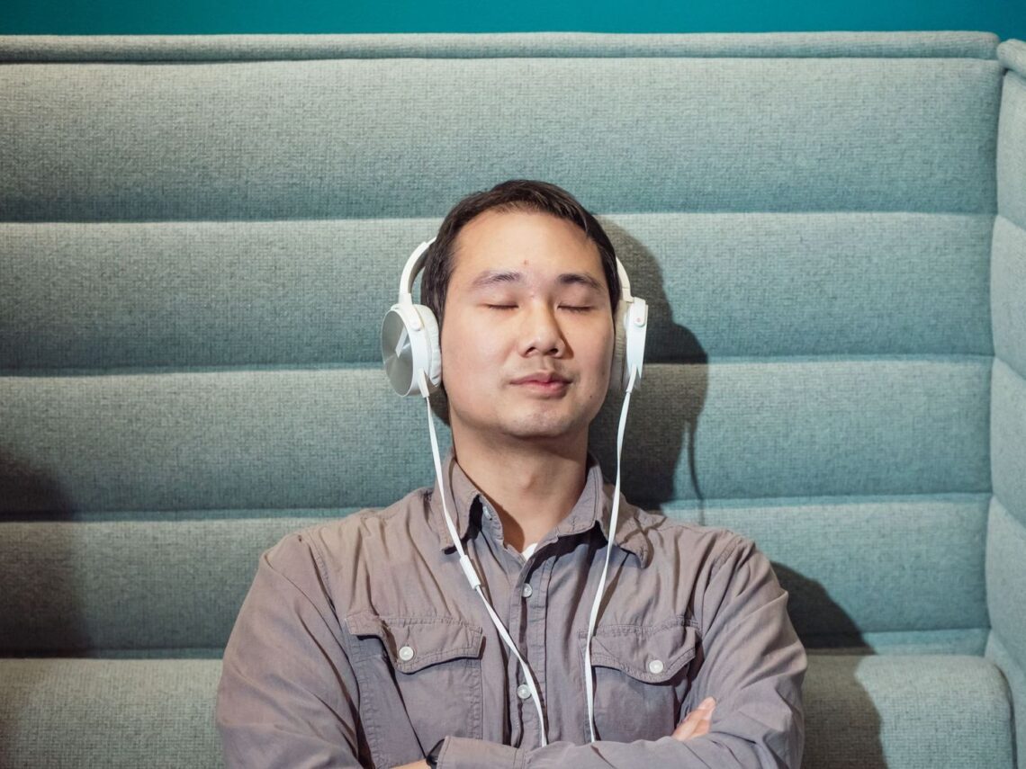 Silmät sulkenut mies kuuntelee musiikkia valkoisilla kuulokkeilla